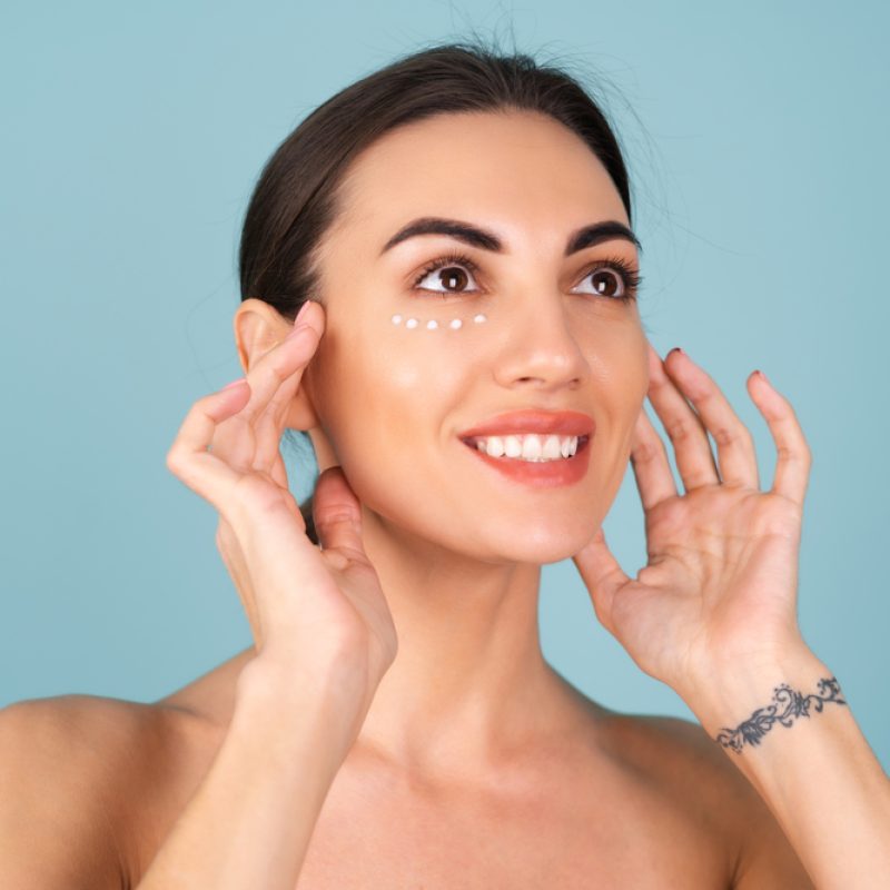 Close-up beauty portrait of a topless woman with perfect skin and natural make-up, with anti-aging cream dots to moisturize and firm the skin under the eyes